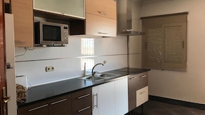Een moderne keuken met een inbouwmagnetron, een roestvrijstalen spoelbak en een raam met zonwering.