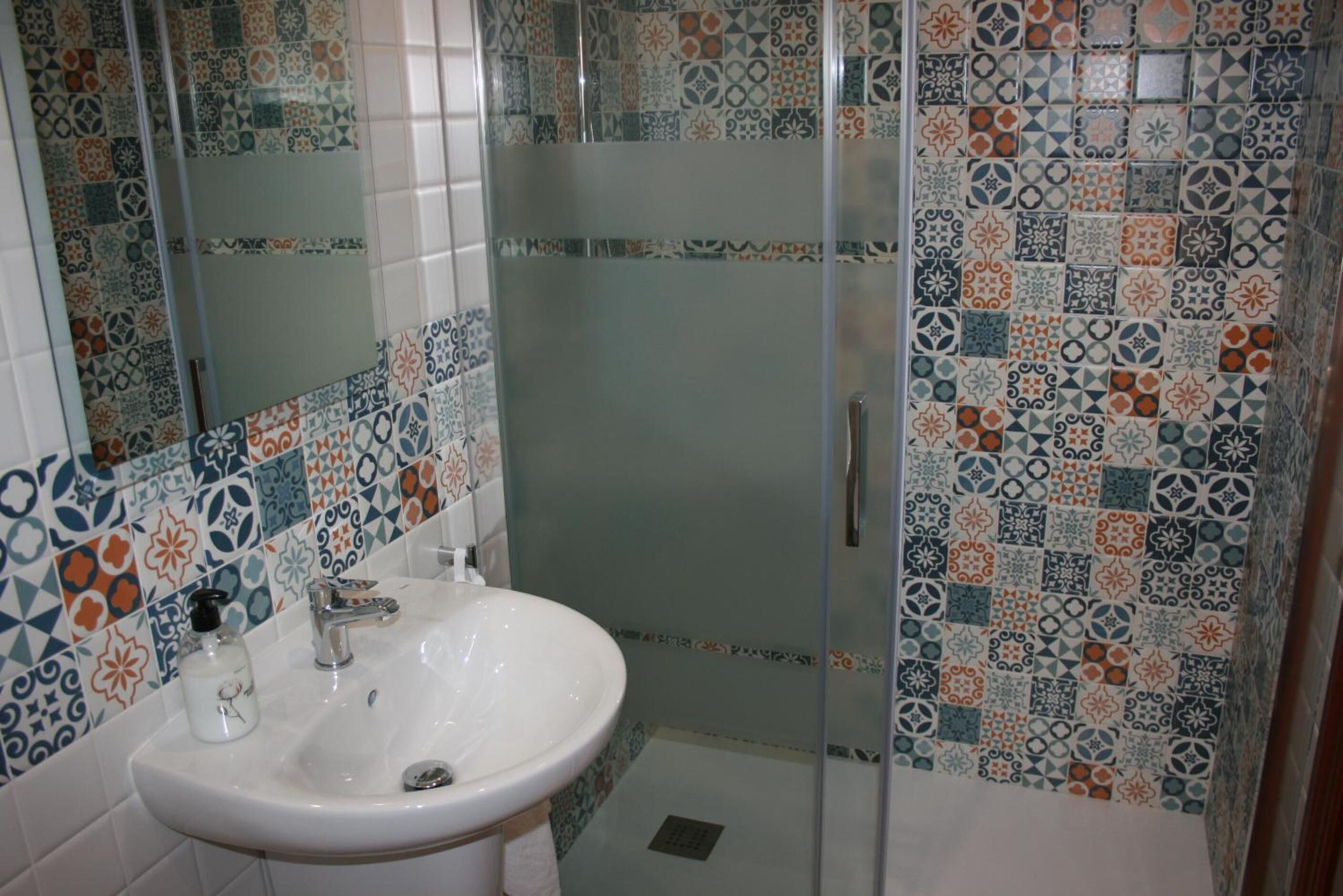 A bathroom with a white sink, a mirror, and a shower area with patterned tiles.