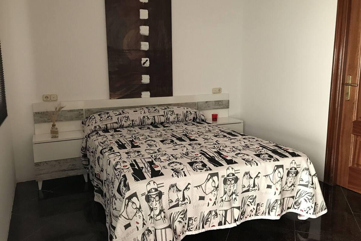 Une chambre à coucher comprenant un lit, une table de chevet, une œuvre d’art accrochée au mur et une porte.