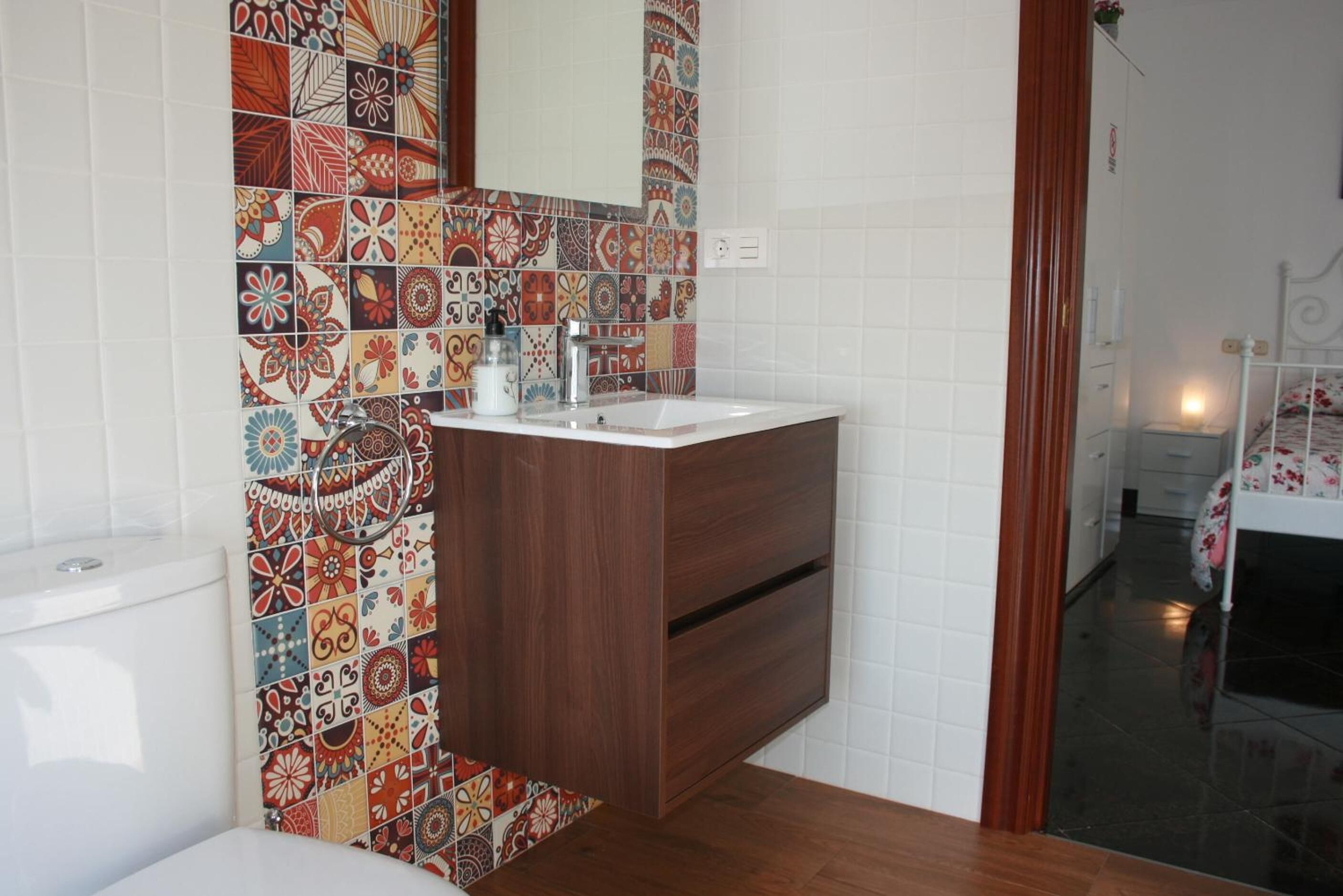 A bathroom with a wooden vanity, a white sink, and a colorful tile backsplash.