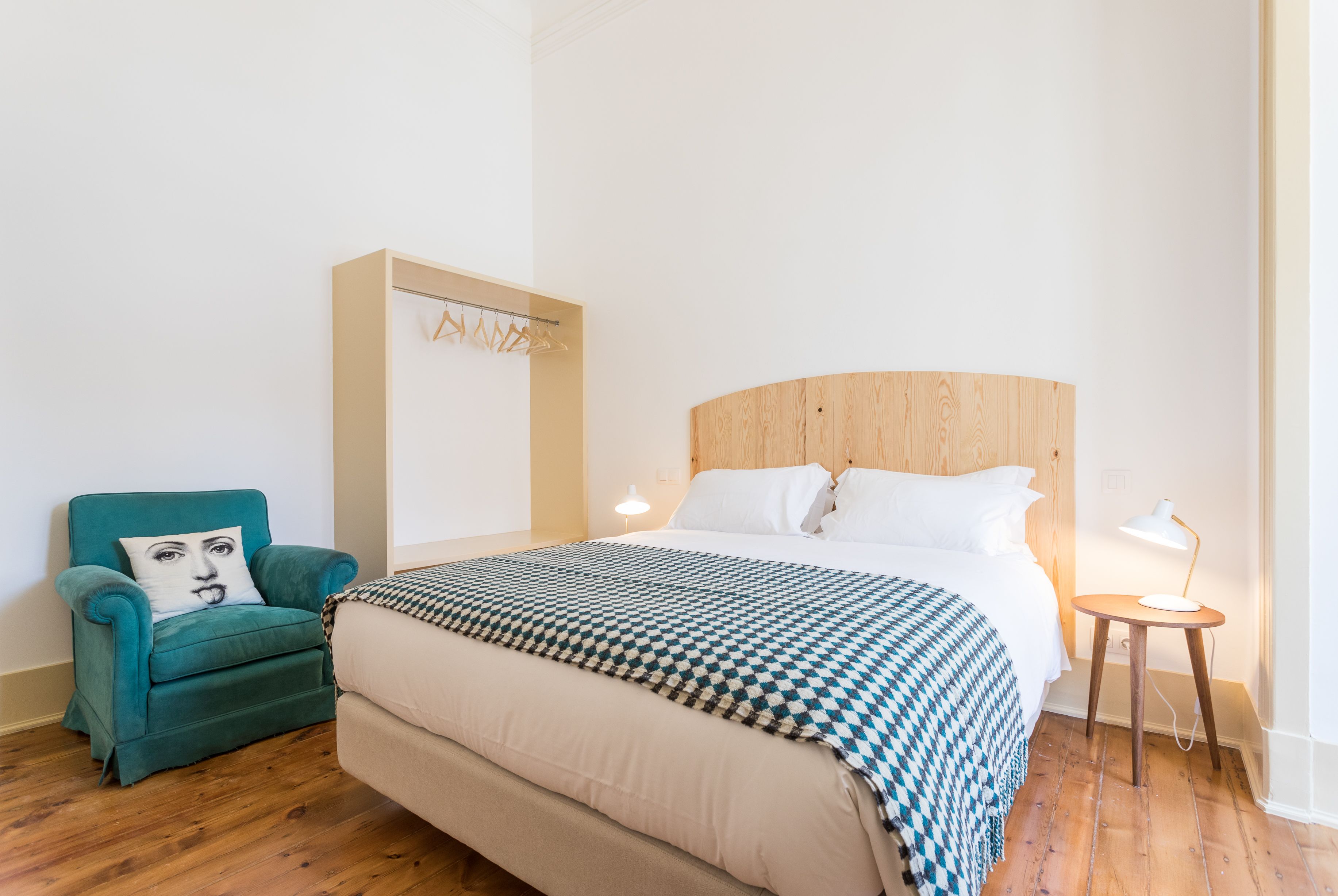 Un dormitorio con cama, una silla, una mesita de noche y un perchero en la pared.