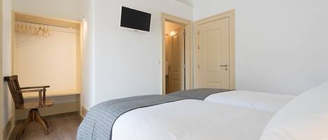A bedroom with two beds, a wooden chair, a TV, and a wardrobe.