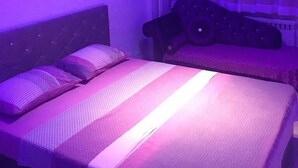 Un dormitorio con cama, almohadas, cabecera, sofá y ventana con cortinas.