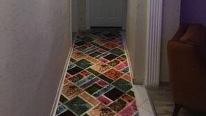 Un pasillo con un suelo de estampado colorido, una puerta blanca al final y una pared morada a la derecha.