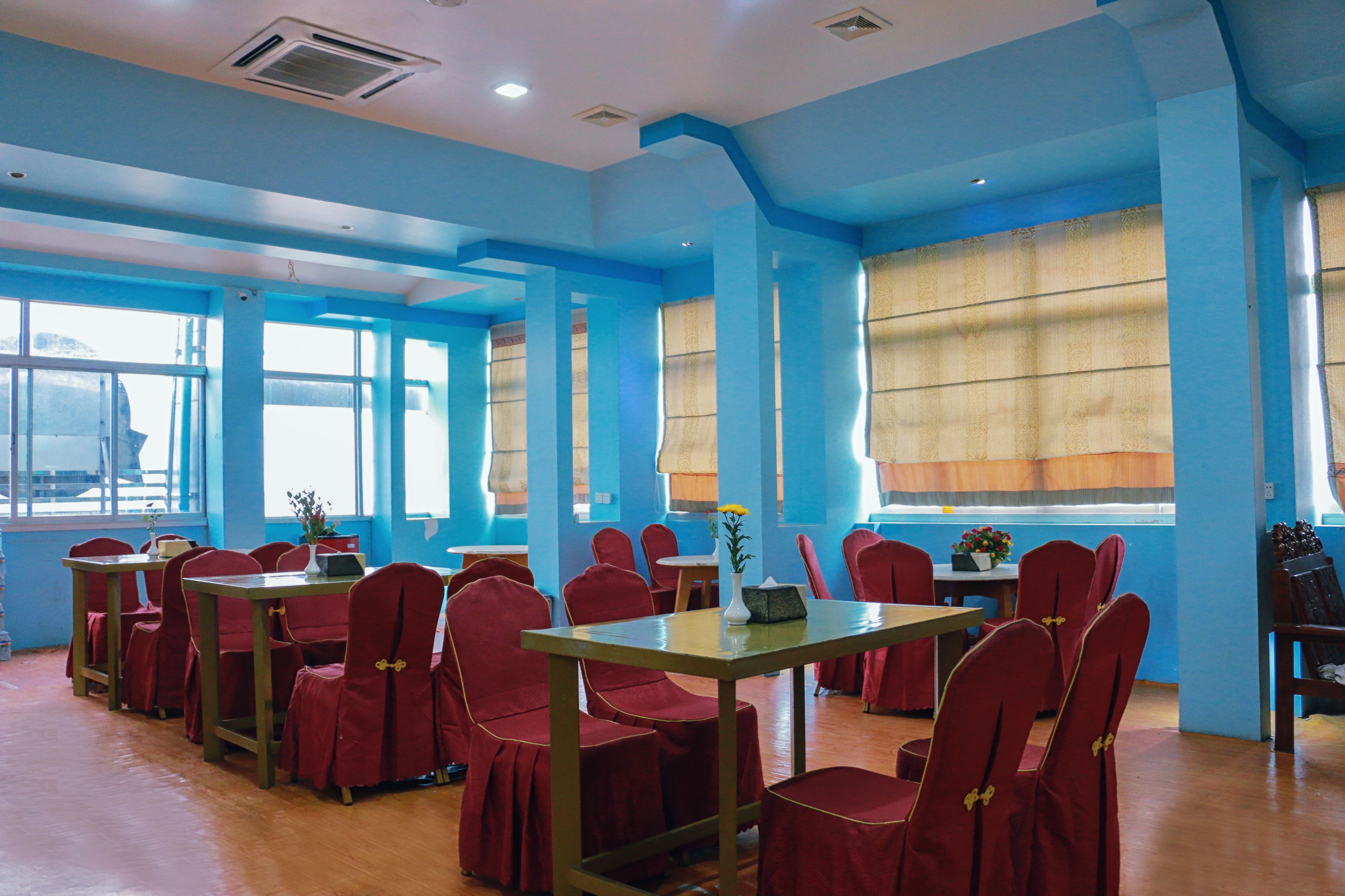 A dining area with red chairs and tables, blue walls, and large windows with curtains.