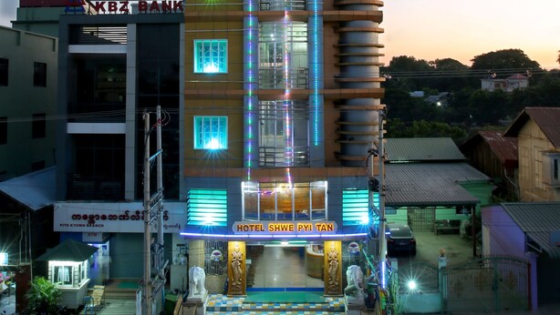 Un hotel de varios pisos con una entrada a cuadros, un letrero llamativo que dice 'Hotel Swee Pyi Tan' y una bandera en la parte superior.
