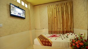 Una habitación de hotel con cama, televisión montada en la pared y ventana con cortinas.