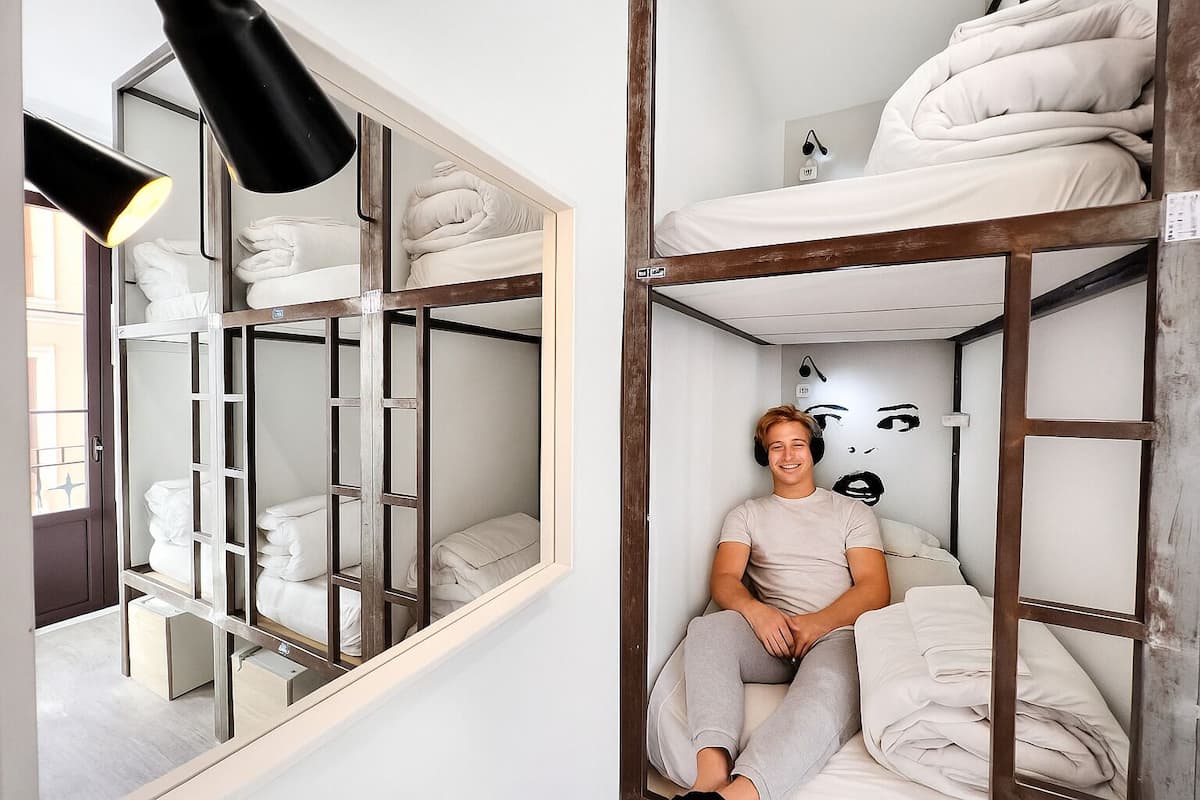 En våningssäng med en spegel, en person som sitter på den nedre våningen och en vägg med en målning av ett ansikte.