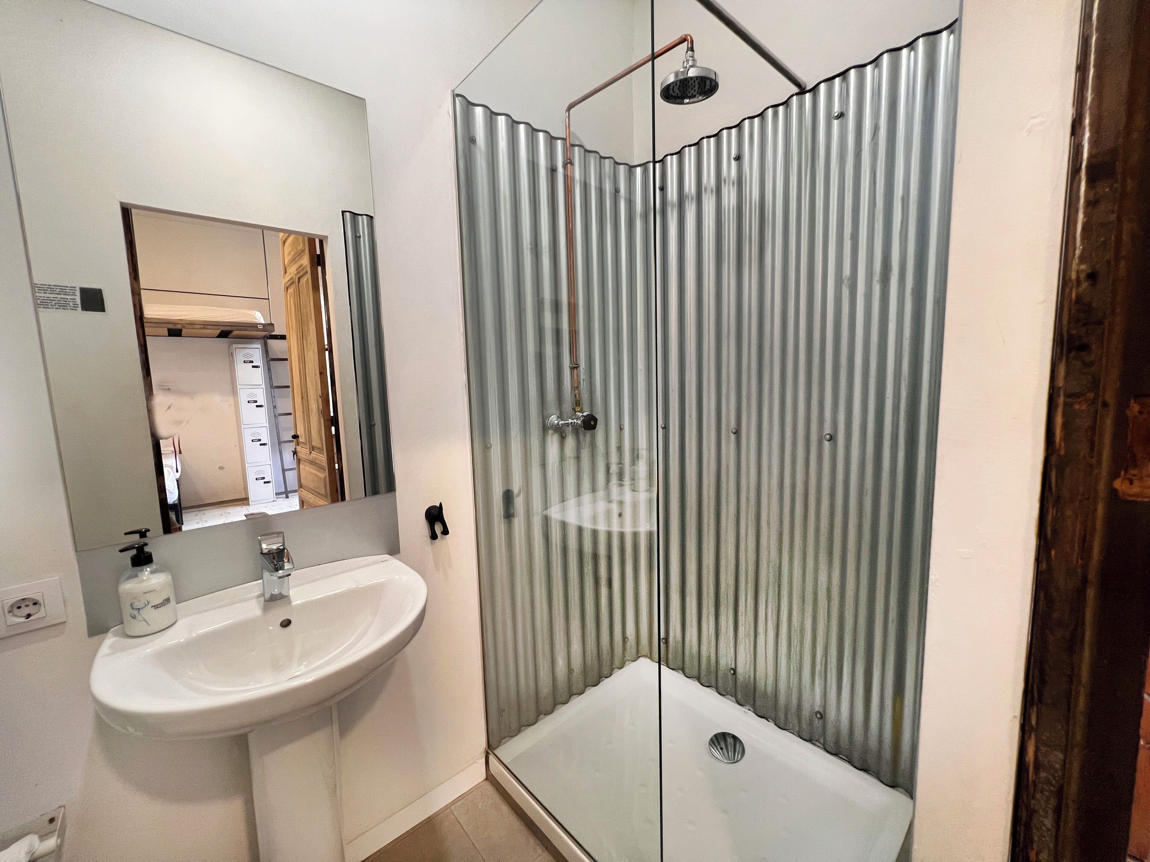 Un baño con un lavabo blanco, un espejo y una ducha con mampara de vidrio.