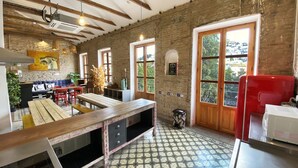 A kitchen with exposed brick walls, wooden beams, a tiled floor, and a red refrigerator. - ECO Hostel (Granada)