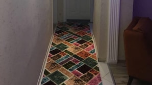 Een hal met een kleurrijk patroon op de vloer, een witte deur aan het einde en een paarse wand aan de rechterkant.