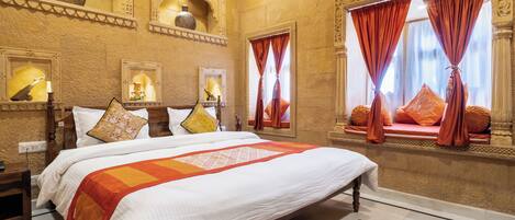 A spacious hotel room with a large bed, ornate wall decorations, and a view of the city through red curtains.