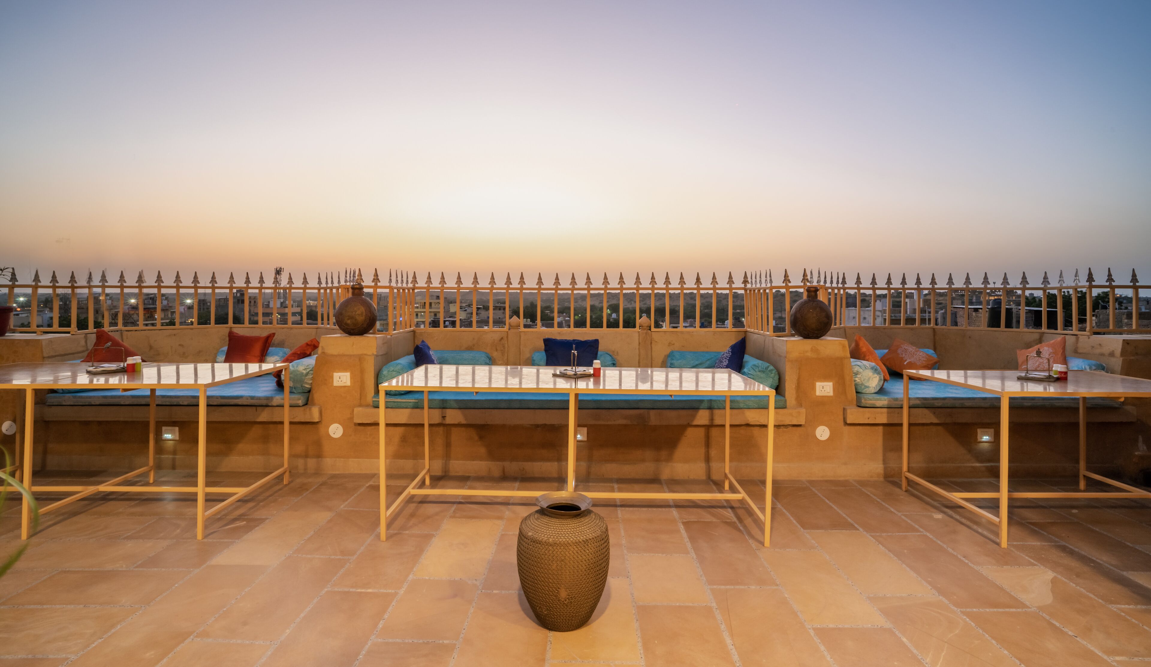 A rooftop terrace with seating areas, a large vase, and a view of the cityscape at sunset.