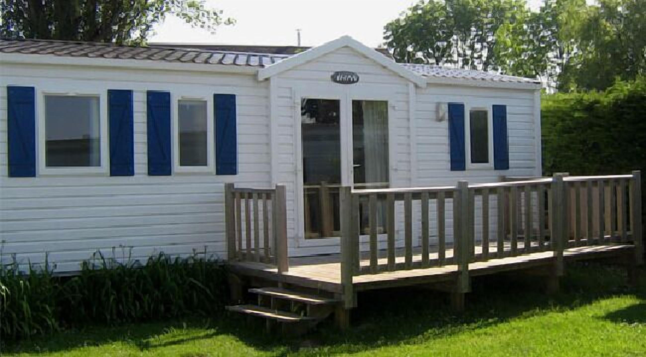 A white mobile home with blue shutters, a porch, and a small deck.