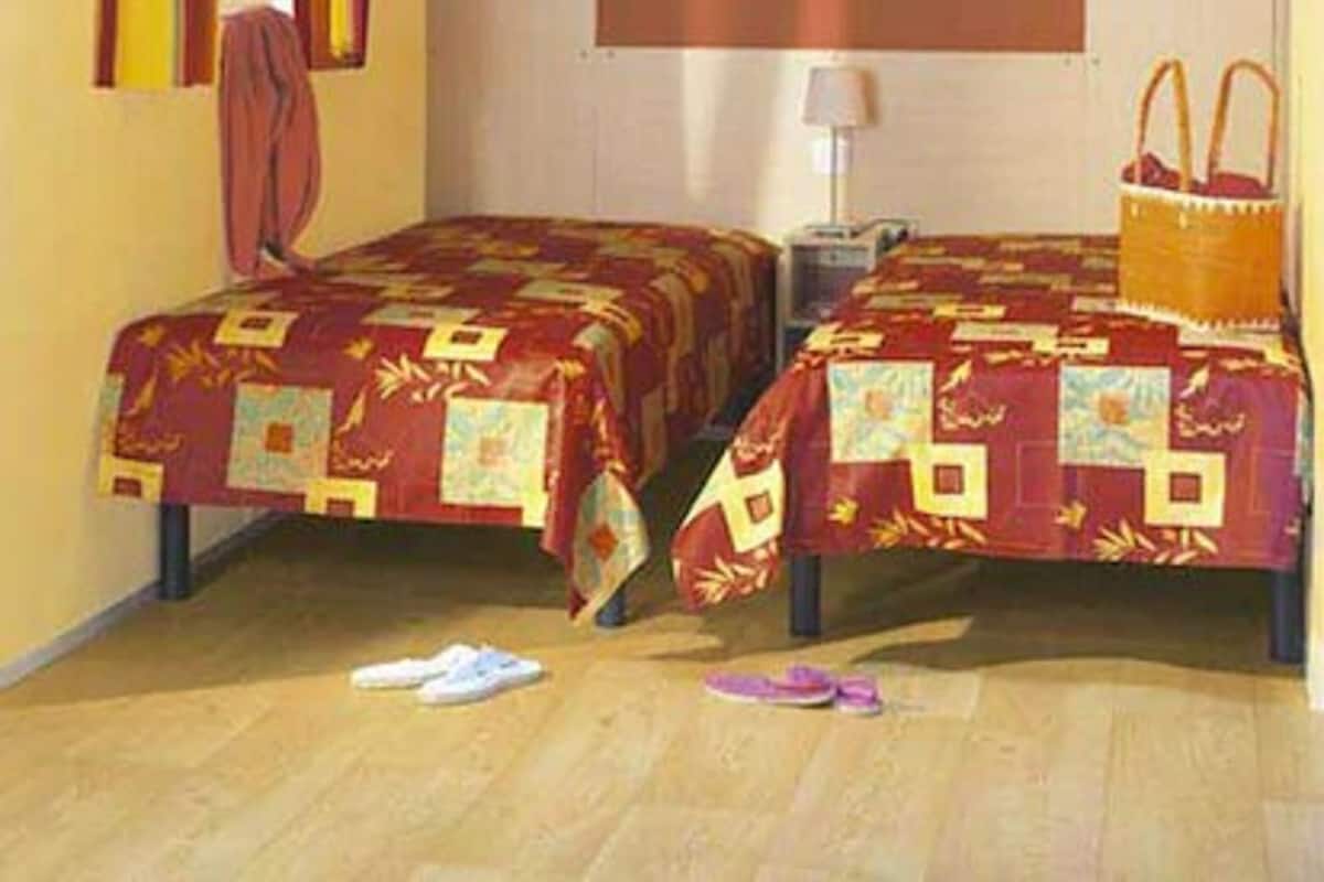 A room with two beds, a window with curtains, a lamp, and a basket on the floor.