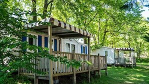 Una casa móvil con terraza de madera y toldo a rayas, rodeada de abundante vegetación.