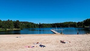 Una playa con un muelle que se adentra en un lago, rodeada de árboles.