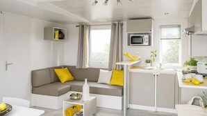 Un espacio habitable compacto con kitchenette, un sofá con cojines amarillos, una pequeña mesa de comedor y un armario blanco.