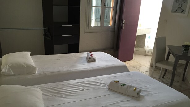 A hotel room with two single beds, a small table, a chair, and a door leading to a balcony. - Hôtel Restaurant Le 8 (Mandelieu-La-Napoule)