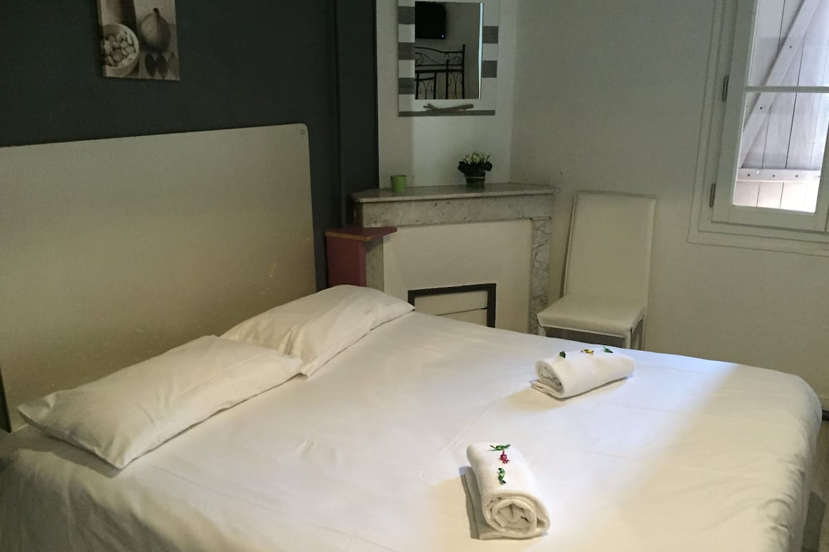 Una cama bien hecha con sábanas blancas y una toalla enrollada con un diseño floral.