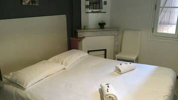 Un lit bien fait, avec du linge de lit blanc et une serviette enroulée ornée d’un motif floral.