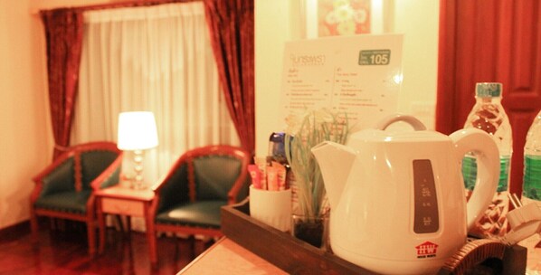 A hotel room with a wooden table, a white kettle, a lamp, and two green chairs. - Patumwan House (Bangkok)