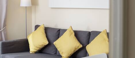A grey sofa with three yellow cushions, a white lamp, and a laptop on a glass table.