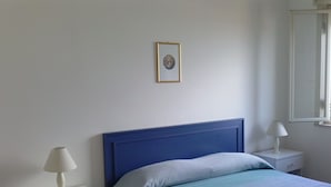 A bedroom with a single bed, a bedside table with a lamp, a nightstand, and a framed picture on the wall. - Fenice Beach Apartment (Castelvetrano)