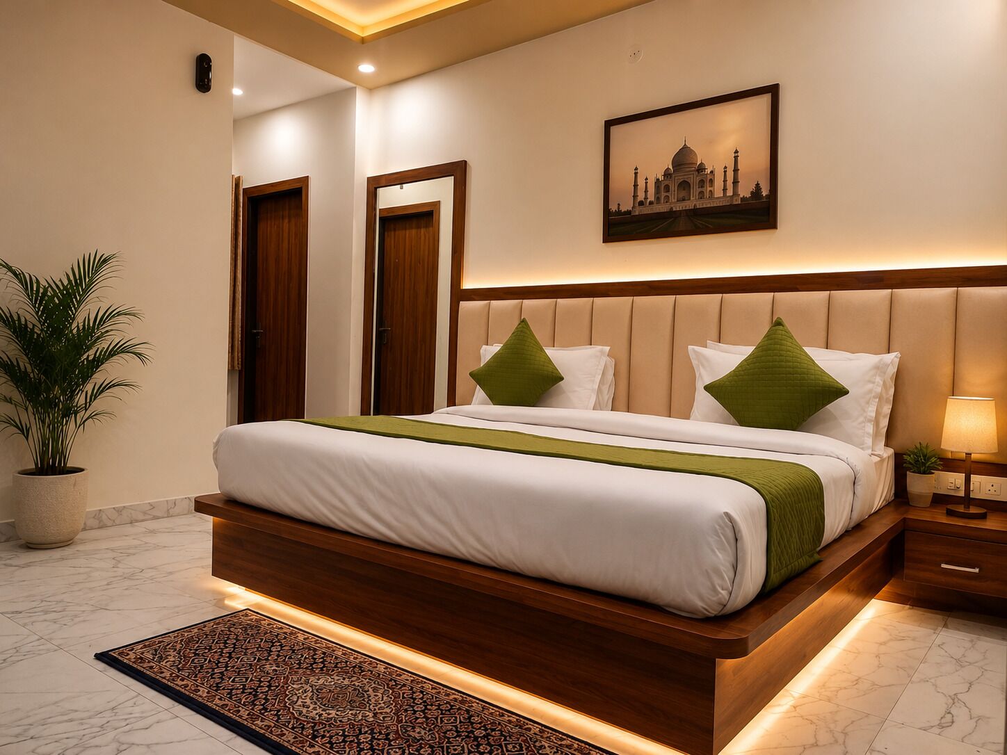 A hotel room with a large bed, a nightstand, a lamp, a potted plant, and a framed picture on the wall.
