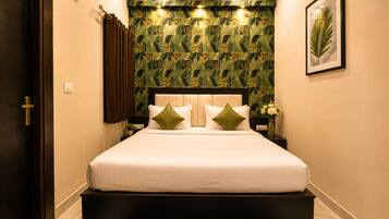 Habitación de hotel con cama, cabecera, mesita de noche, aire acondicionado montado en la pared, un cuadro enmarcado y una puerta.