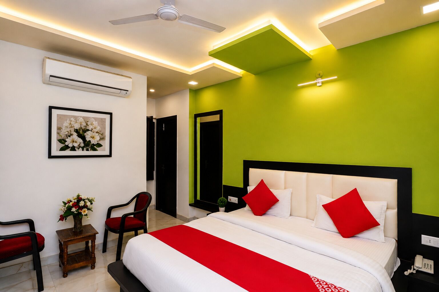 A hotel room with a bed, a chair, a small table with a vase of flowers, and an air conditioning unit.