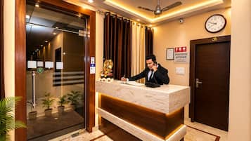 En hotelreception med receptionist, et ur og skilt til Paradise Kitchen.