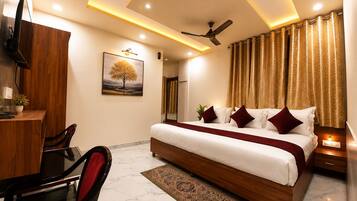 A hotel room with a large bed, a desk, a chair, a ceiling fan, and a painting on the wall.