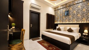 Quarto de hotel com cama, escrivaninha, cadeira, ar condicionado e detalhe decorativo na parede.