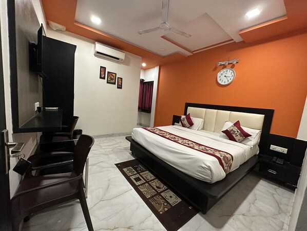 A bedroom with a bed, a desk, a chair, a ceiling fan, an air conditioner, and a clock on the wall. - Hotel Aaradhya Residency (Agra)