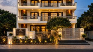 Hotel com vários andares, design moderno, com varandas, entrada bem iluminada e jardim frontal ajardinado.
