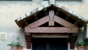 Fachada de piedra con una puerta doble negra, un pequeño escalón que lleva a la entrada y dos macetas a cada lado.