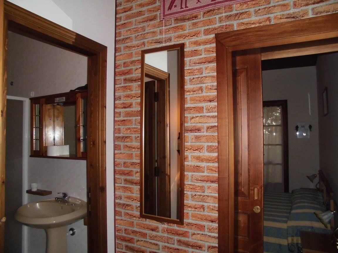 Une salle de bain avec un lavabo et un miroir, une porte en bois et un mur en briques.