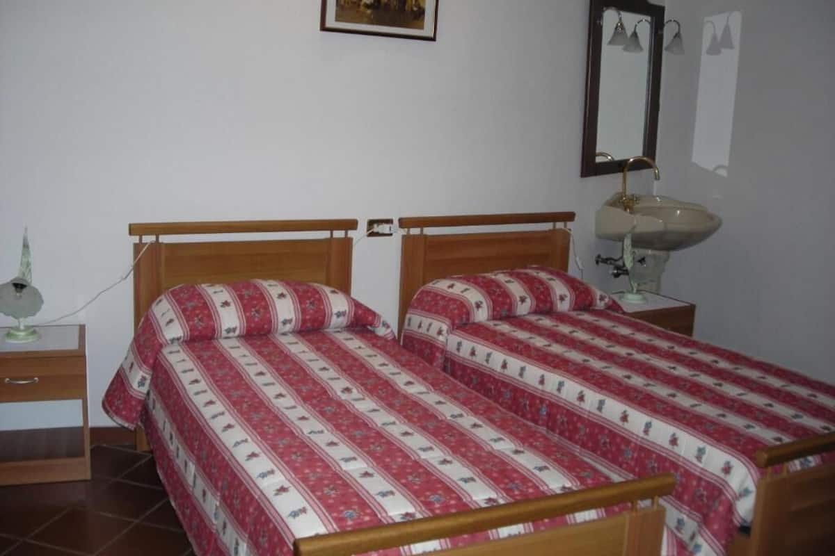 A bedroom with two single beds, a bedside table with a lamp, a mirror, and a framed picture on the wall.