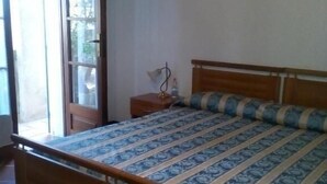 Un dormitorio con una cama de madera, una mesita de noche, una lámpara y una ventana con vistas al verdor.
