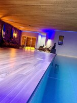 Una piscina interior moderna con suelo de madera e iluminación azul.