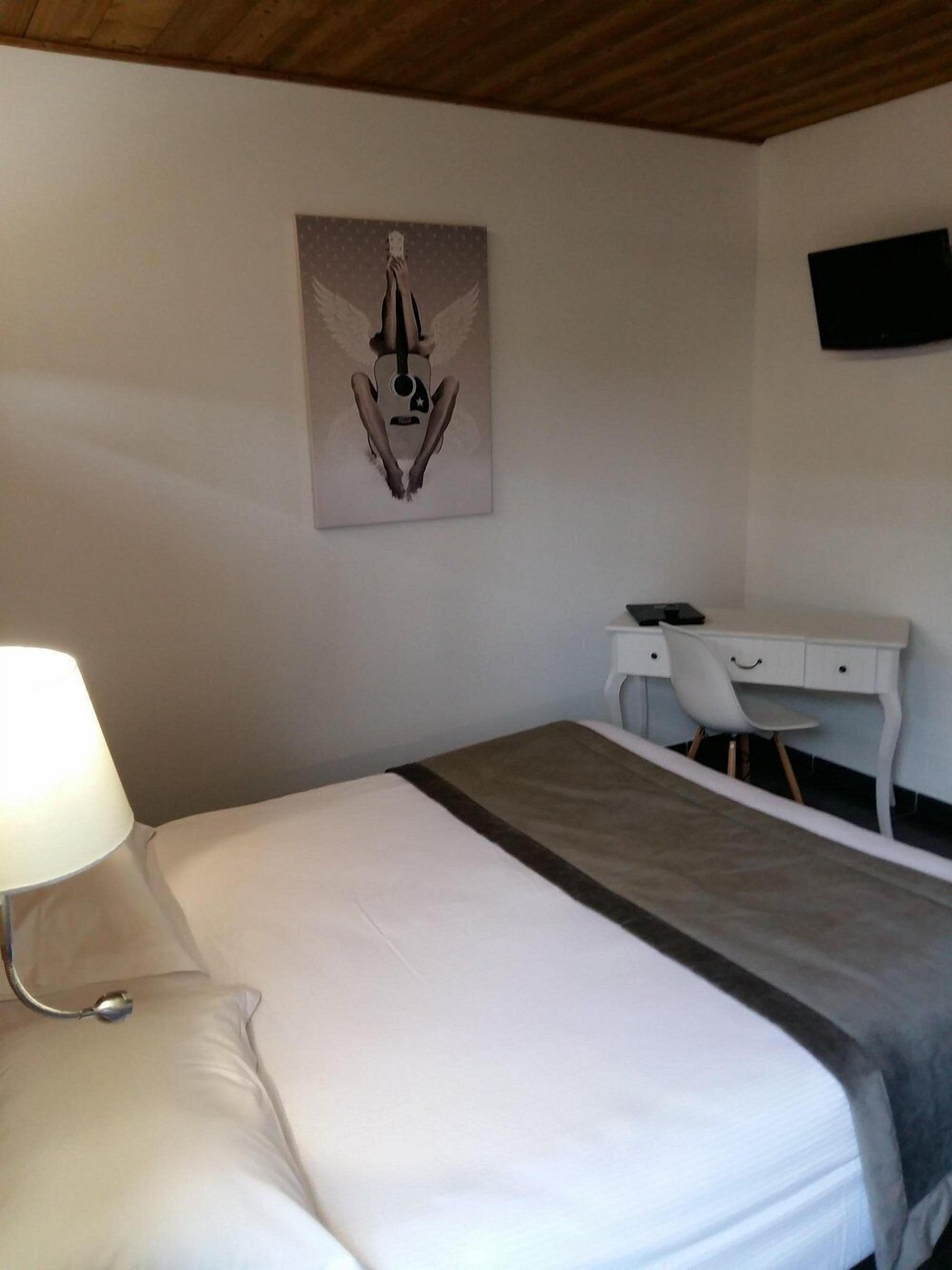 Een hotelkamer met een bed, een bureau, een stoel, een lamp en een aan de muur bevestigde televisie.