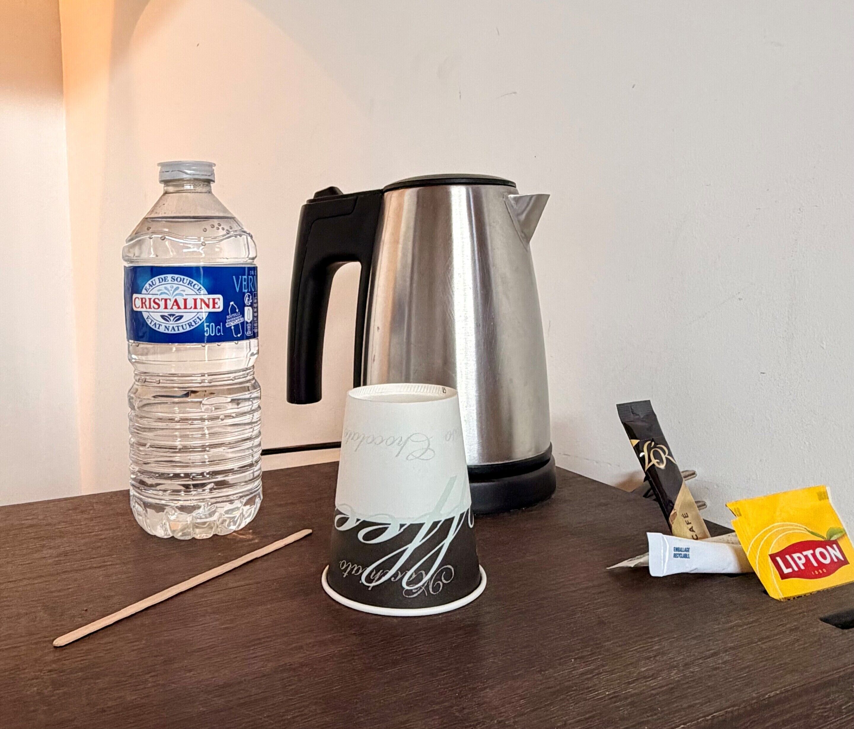 A table with a water bottle, a coffee cup, a kettle, and Lipton tea packets.