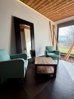 Una sala de estar moderna con dos sofás azul verdoso, una mesa de centro de madera y un ventanal que ofrece vistas a un jardín y montañas.