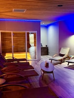 Una habitación con piso de madera, un área de estar con sillas y una mesa, y vista a un espacio exterior a través de un ventanal.