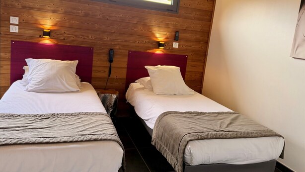 A room with two beds, each with a headboard and bedside lamps. There is a window above the beds, and a telephone mounted on the wall. - Bio Motel (Saint-Vulbas)