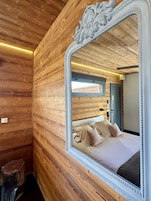 Un dormitorio con paneles de madera, un espejo grande y ornamentado, una cama con almohadas y una puerta al fondo.