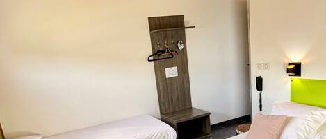 A hotel room with two single beds, a wooden wardrobe, a ceiling fan, a telephone, and a bright green headboard.