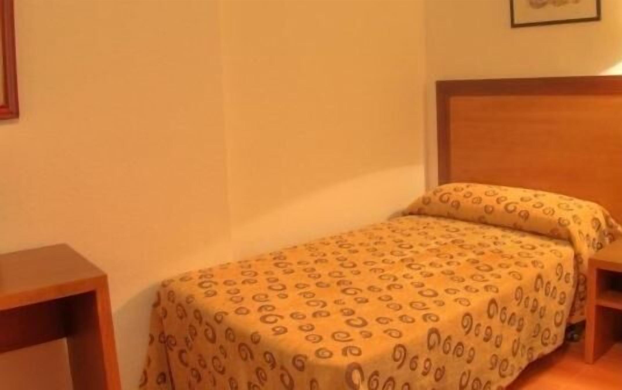 Un lit simple avec une couvre-lit à motifs, une tête de lit en bois et des tables de chevet de chaque côté.