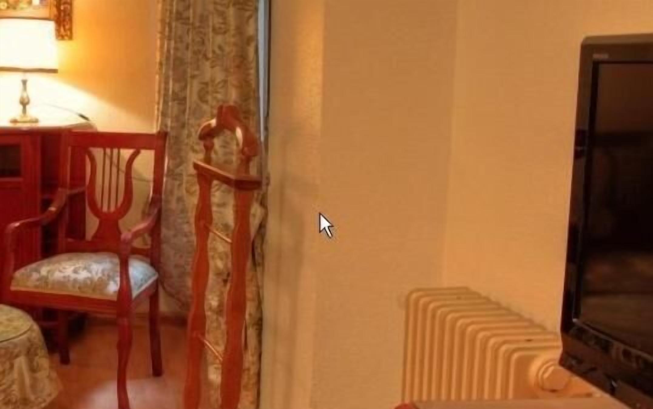 A room with a wooden chair, a table, a lamp, and a radiator.